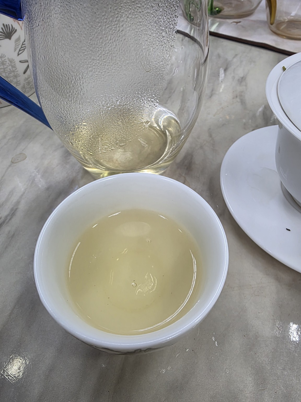 Pale yellow Huoshan Huangya liquor from the second infusion in a white porcelain cup, with a glass pitcher and gaiwan.