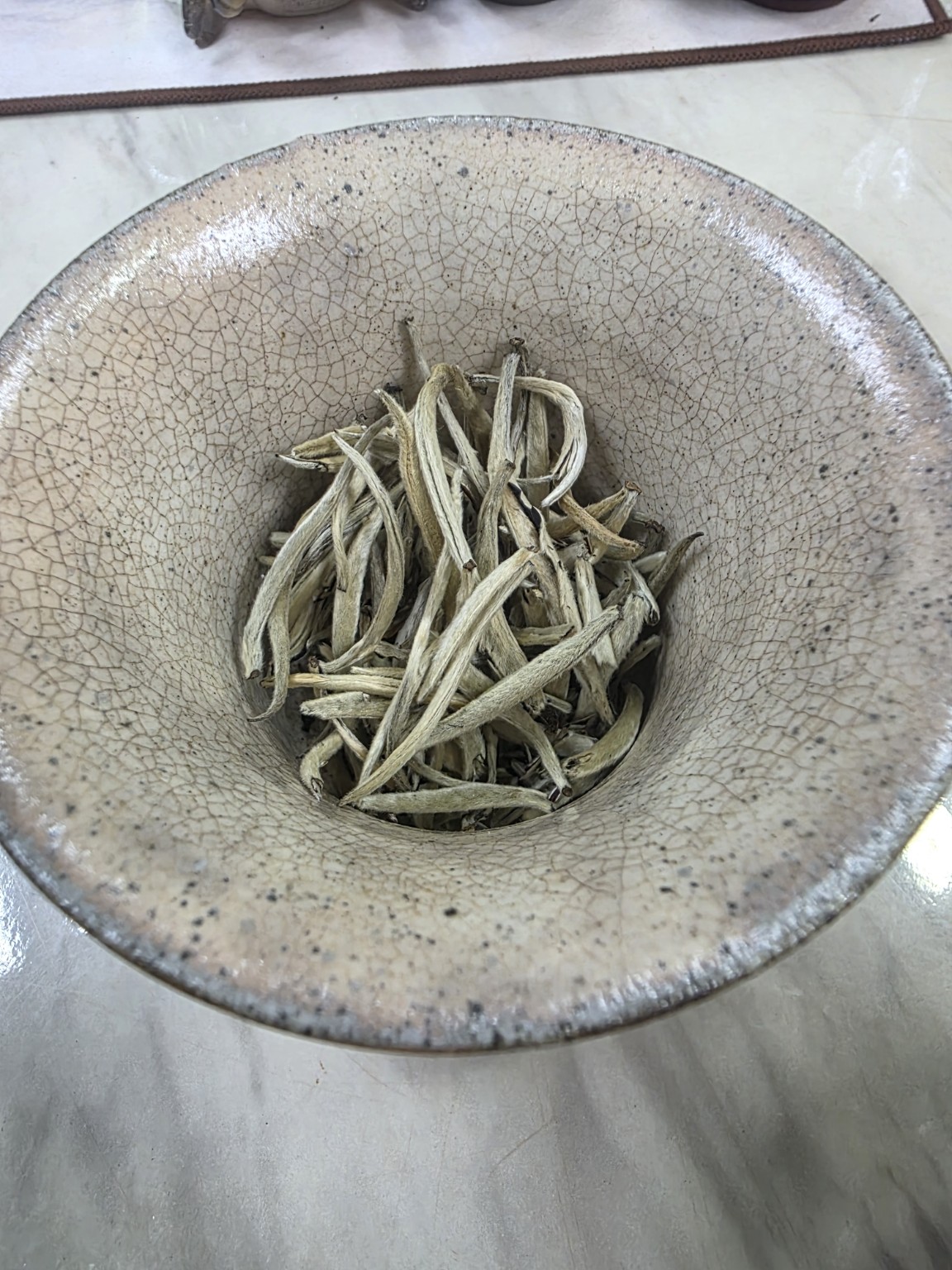 Pale silver and straw-gold dry tea buds in a crackle-glazed gaiwan